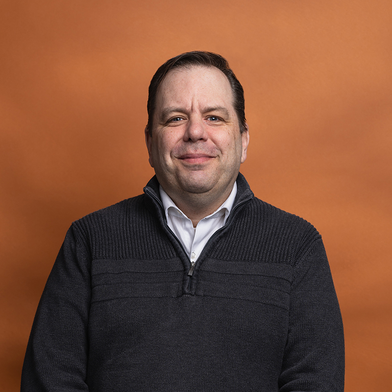 Headshot of Geoffrey Meier with orange background