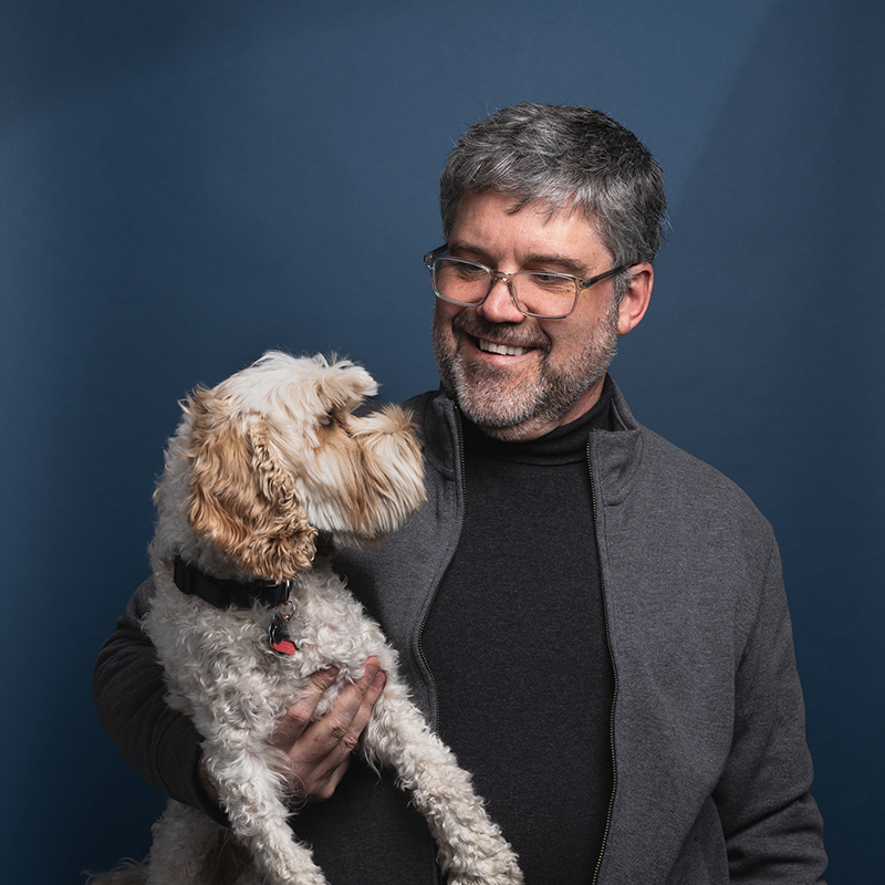 Headshot of Jeff Millett and his dog with blue background